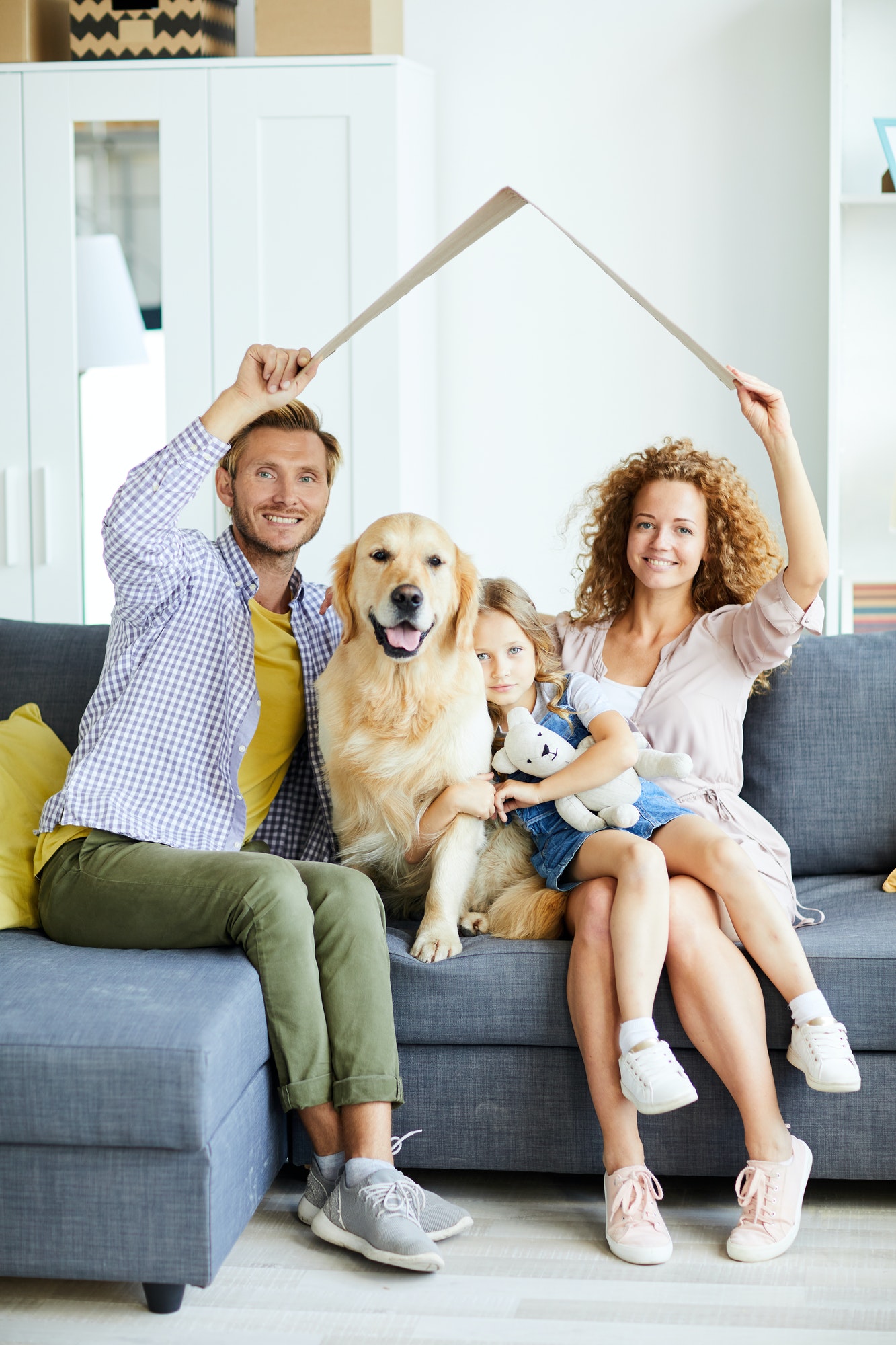 Happy young family with their daughter and golden retriever sitting on a couch, symbolizing home ownership and comfort through First Home Buyer Loans.