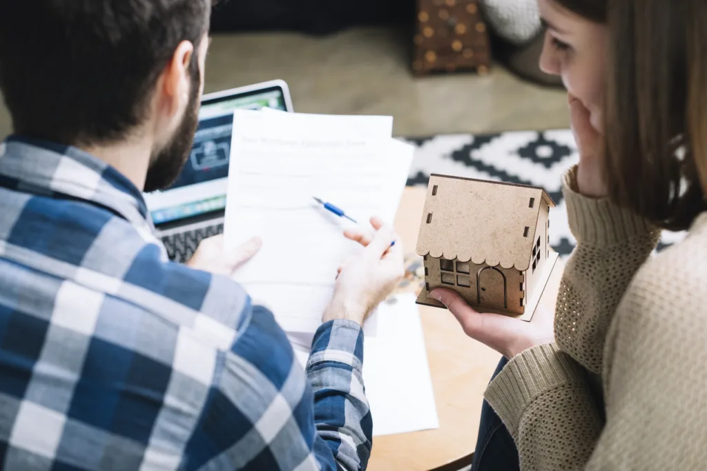 A couple reviews a mortgage application form while holding a model house, representing planning and eligibility for First Home Buyer Grants in Australia.